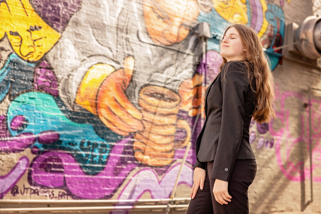 A close-up portrait using the natural light, brightly colored mural, and brick textures of a Lawrence alley.
